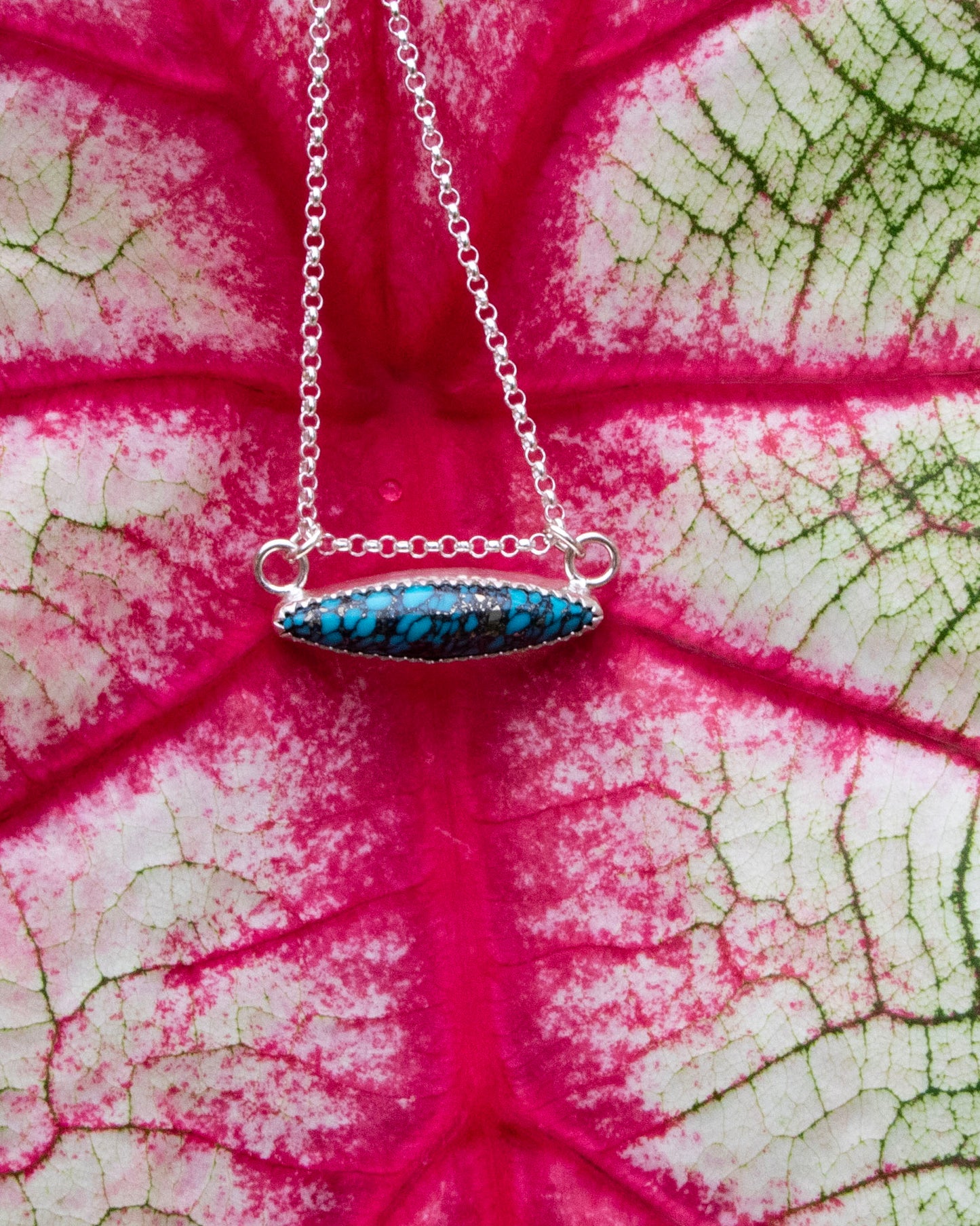 mermaid's scale horizontal marquise stone sterling silver necklace in front of red vains of white and green leaf