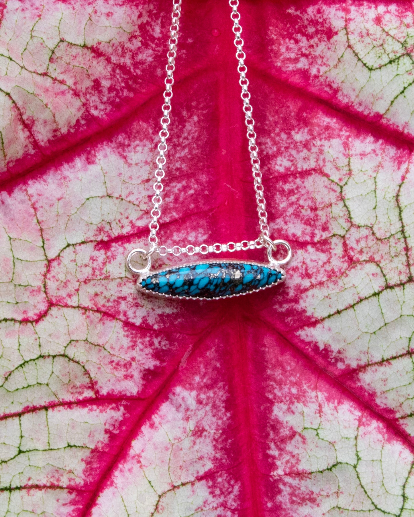 mermaid's scale horizontal marquise stone sterling silver necklace in front of red vains of white and green leaf