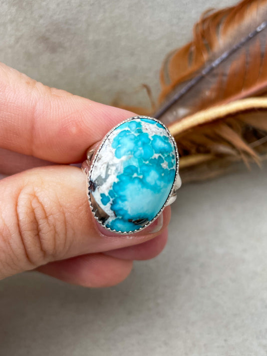 oval high-grade, high-dome white water turquoise ring with natural pyrite flecks set in a serrated bezel on a split-shank band