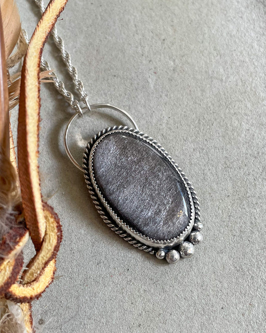 handcrafted statement necklace with oval silver sheen obsidian in a serrated bezel with twist border and hand forged accent beads on an oversized full circle bail and and french rope chain