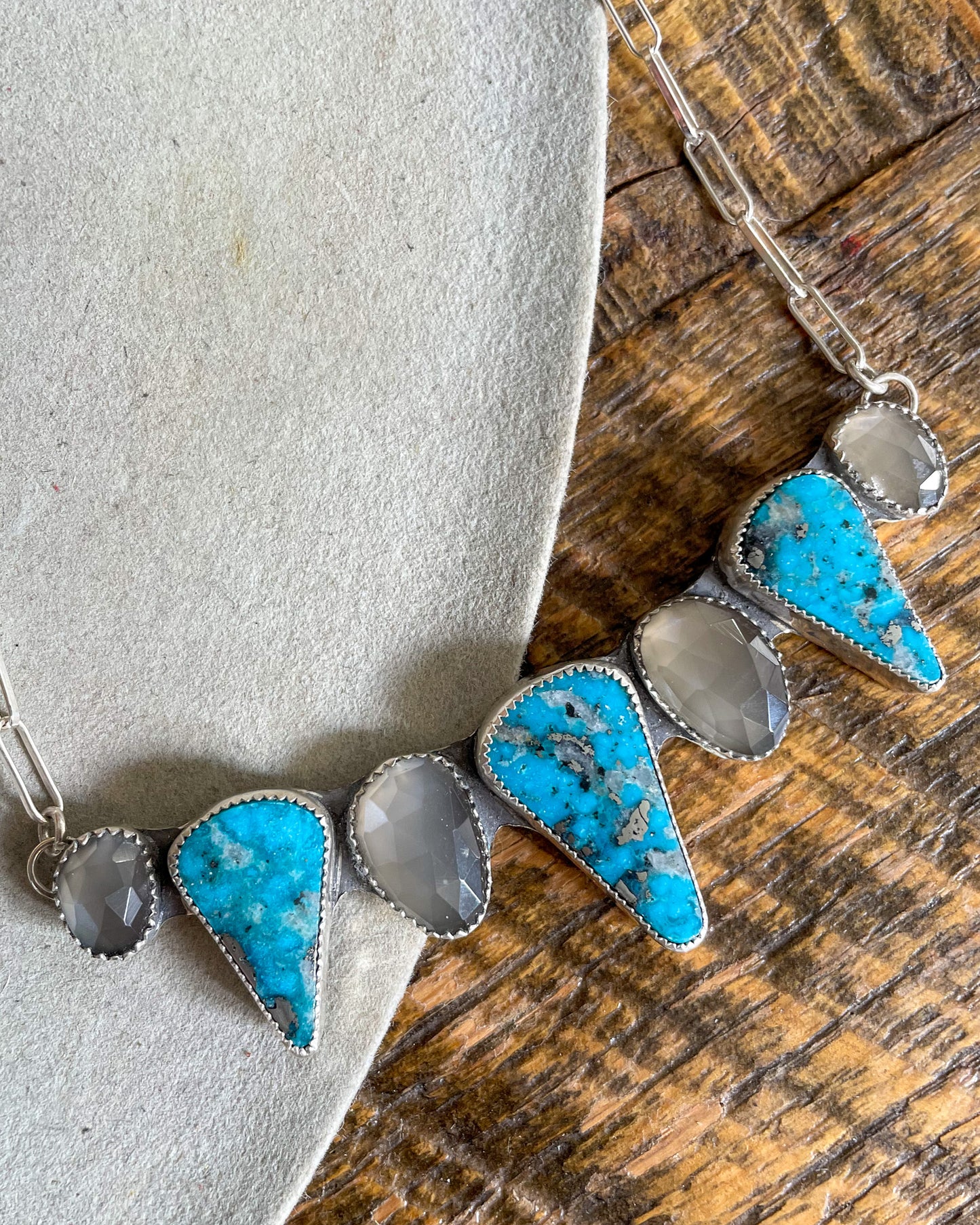 handcrafted chest collar necklace with alternating grey moonstone and triangular ithica peak turquoise pointing down. silver paperclip chain attaches at each end