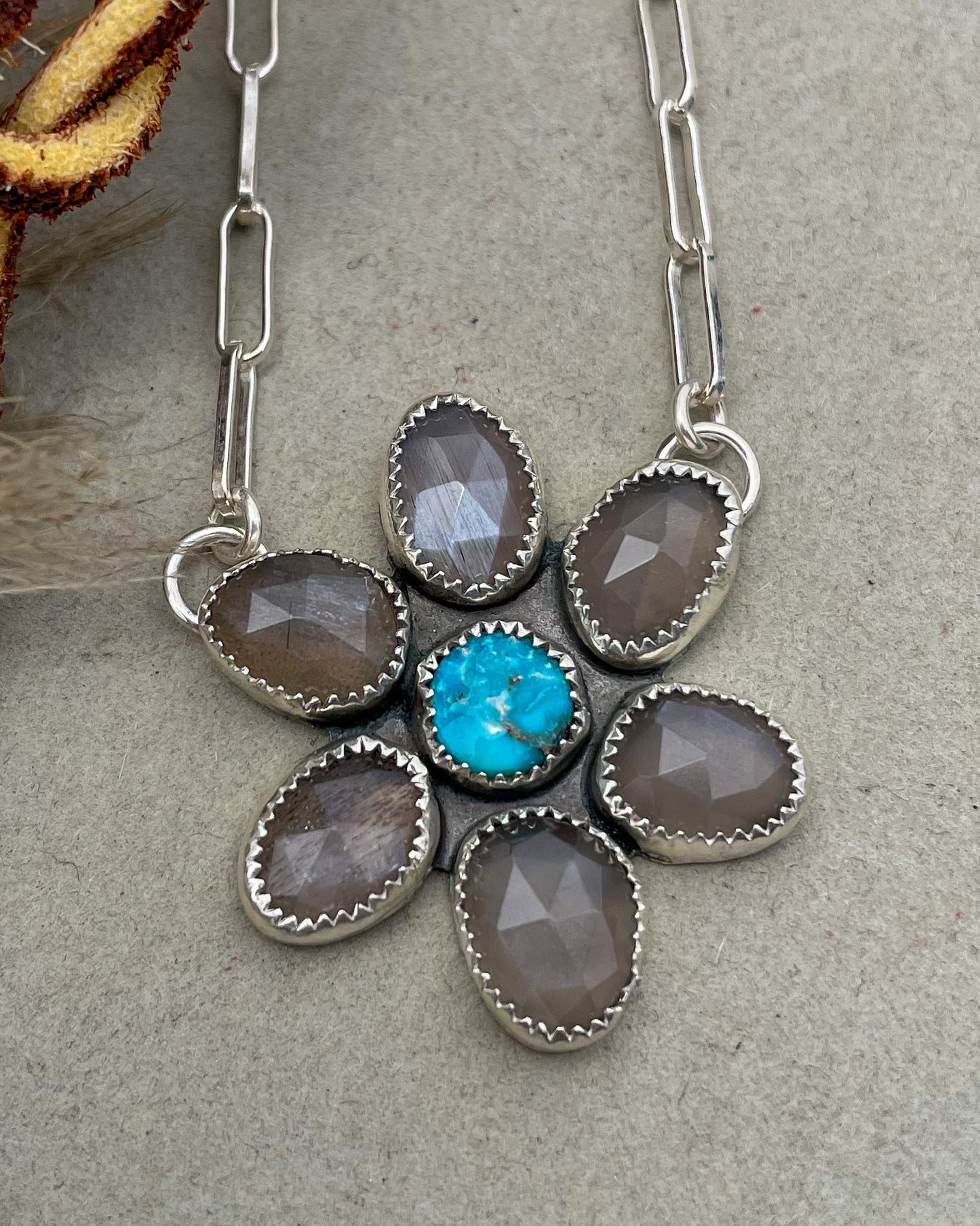 handcrafted flower pendant with center turquoise cabochon and six grey moonstone rosecut pedals attached by jump rings on two pedals to paperclip chain