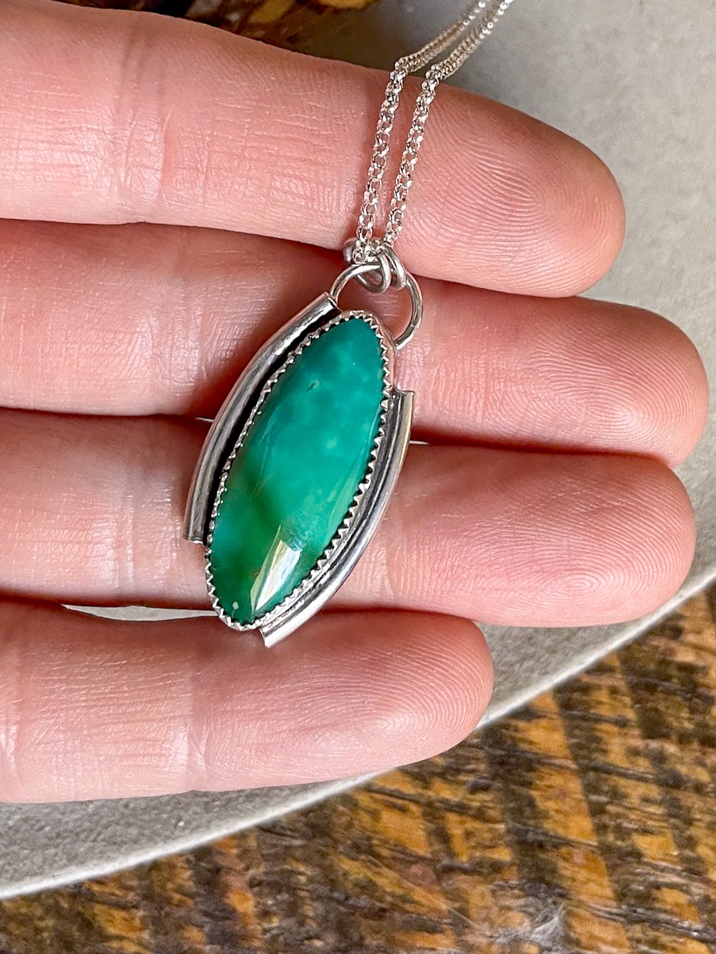 green marquise Kingman turquoise necklace with offset open silver frame on dainty rolo chain held in hand