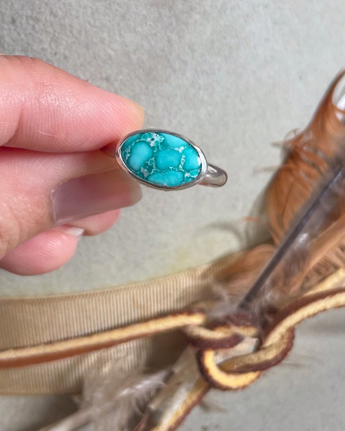 Turquoise stone ring held by a hand with feathers in the background