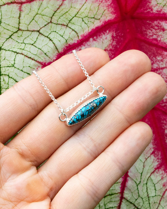 mermaid's scale horizontal marquise stone sterling silver necklace being held in front of red vains of white and green leaf 