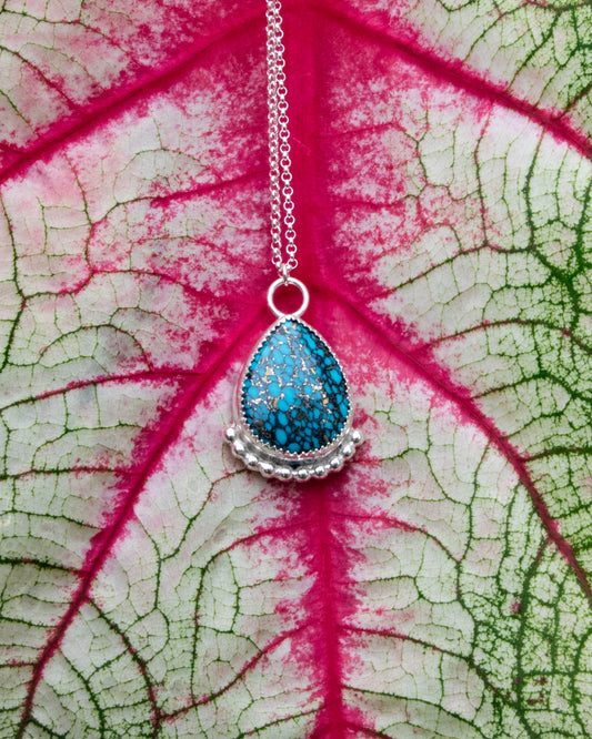 mermaid's scale teardrop stone sterling silver necklace with silver beads along bottom in front of red vains of white and green leaf 
