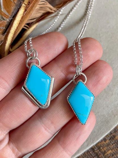 two diamond shaped sleeping beauty pendants on dainty rolo chains held in hand