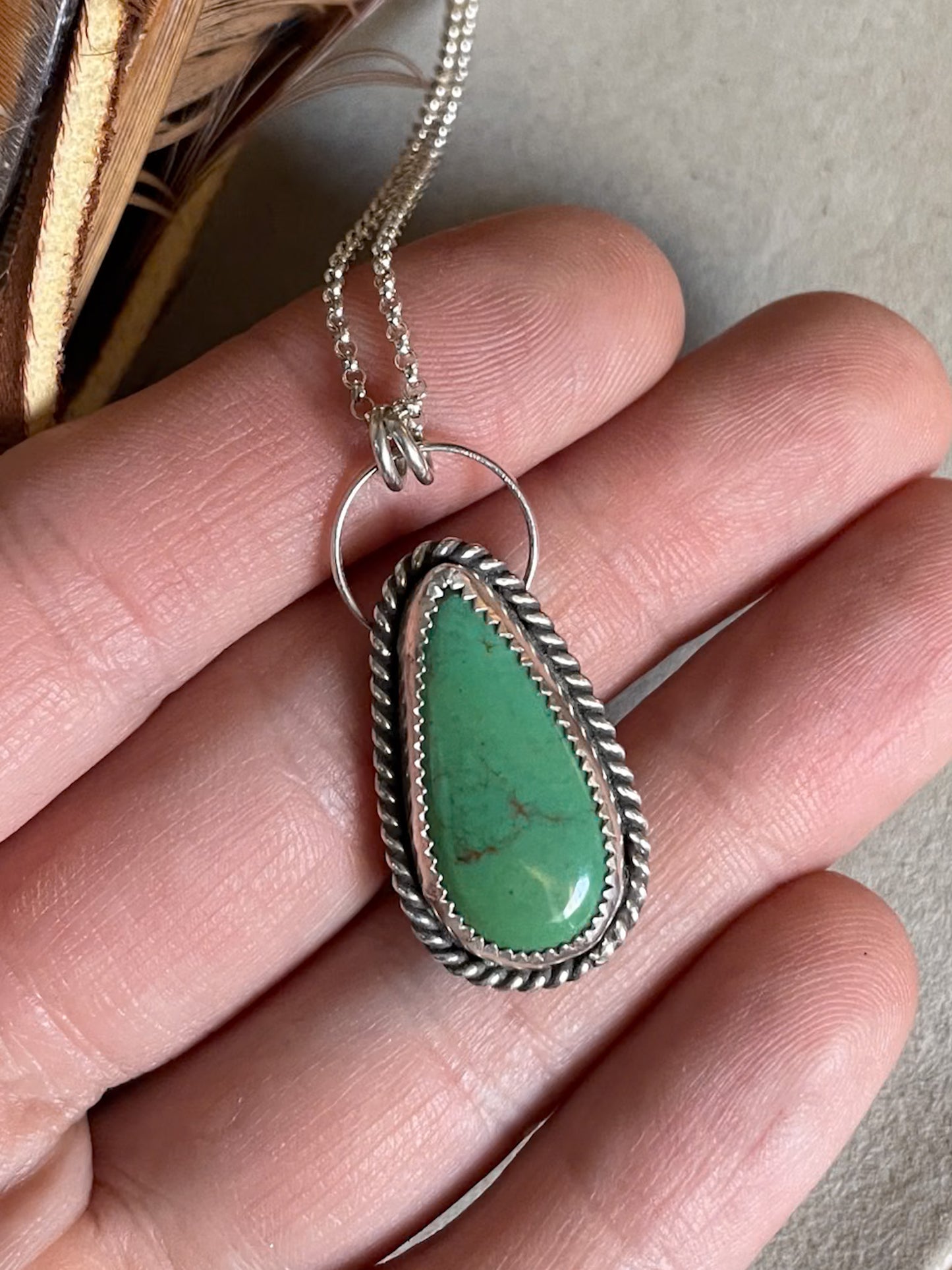 green turquoise mountain necklace with rope border on dainty chain held in hand