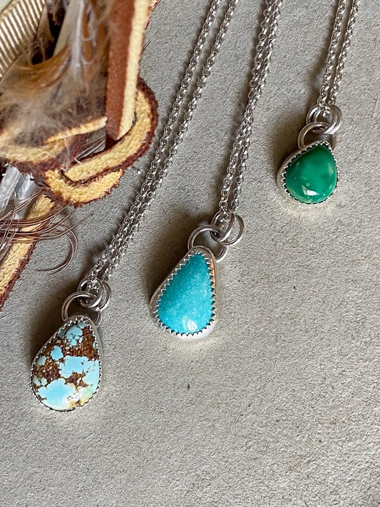 Three necklaces with teardrop-shaped turquoise pendants on dainty rolo chains