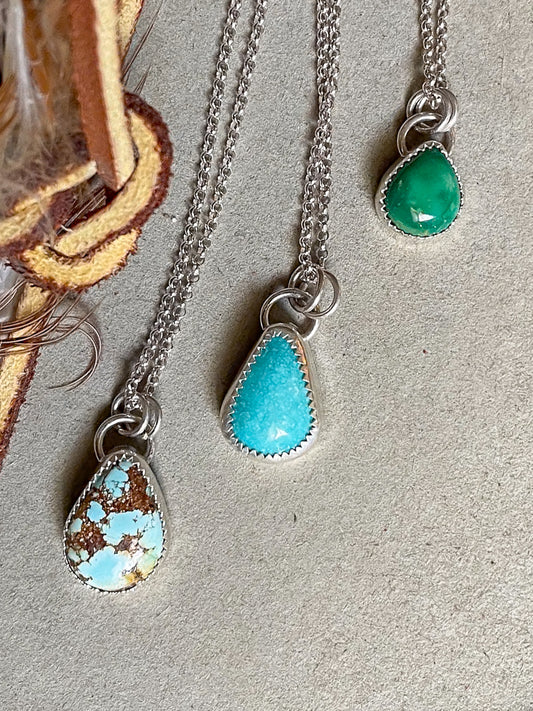 Three necklaces with teardrop-shaped turquoise pendants on dainty rolo chains