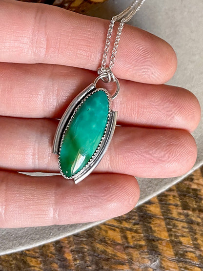 green marquise Kingman turquoise necklace with offset open silver frame on dainty rolo chain held in hand