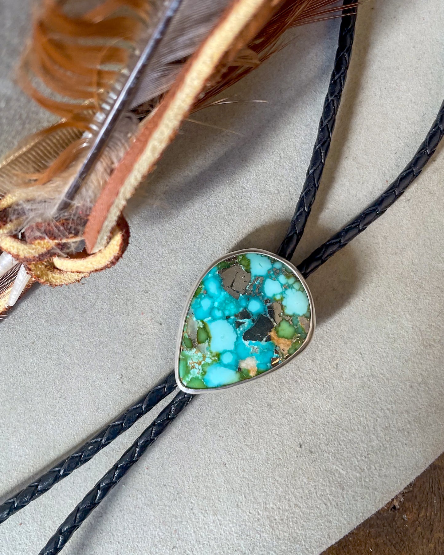 blue and green sonoran gold turquoise with natural pyrite pear cabochon bolo in smooth bezel on black braided cord