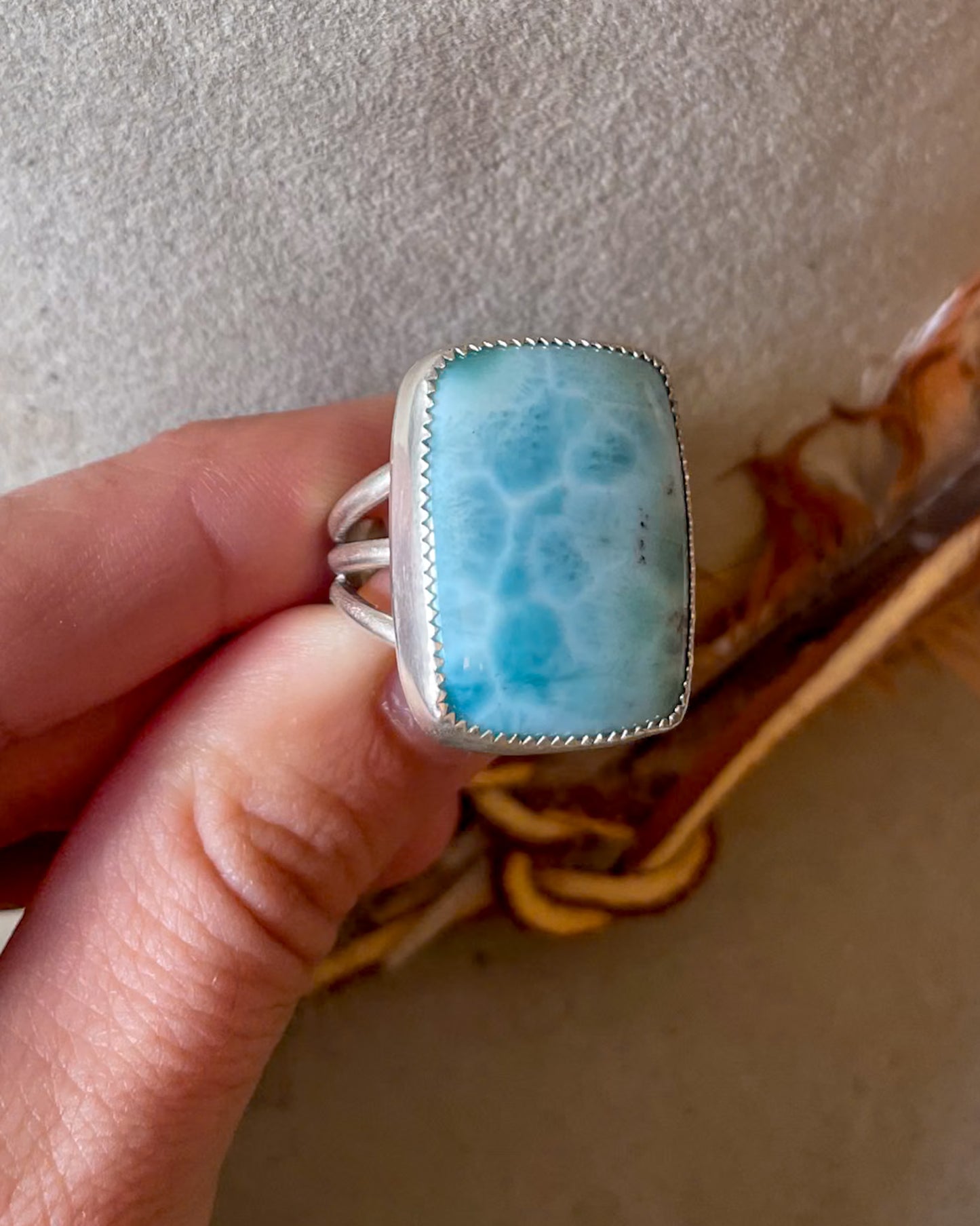 Ring with a blue larimar stone held by a hand against a neutral background