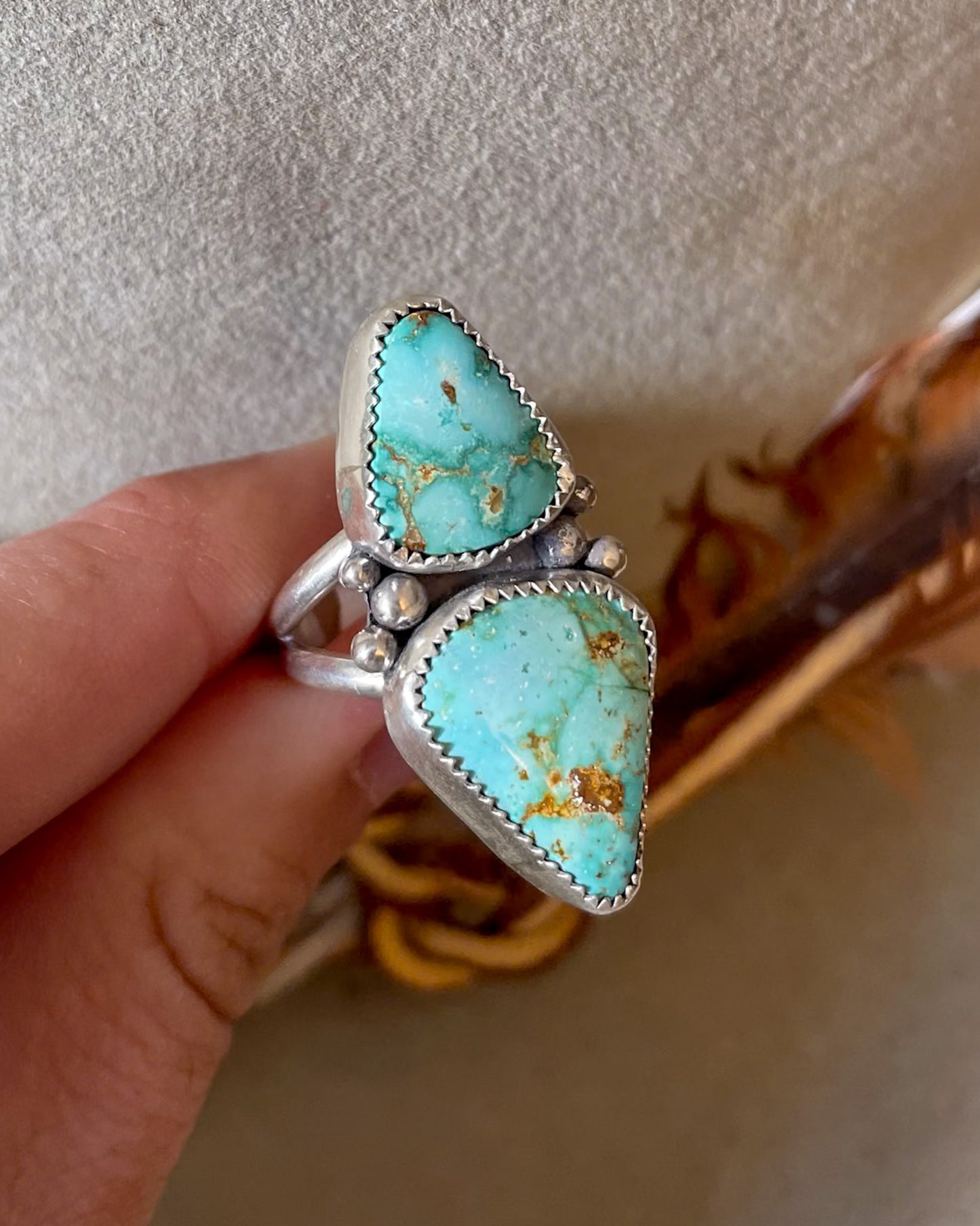 Double Turquoise stone ring with silver setting held by a hand against a neutral background