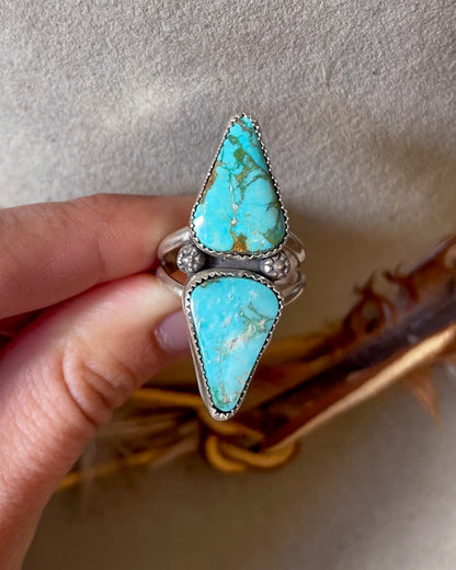 mirrored turquoise mountain turquoise cabochons separated by floral accents on split shank band held in fingers