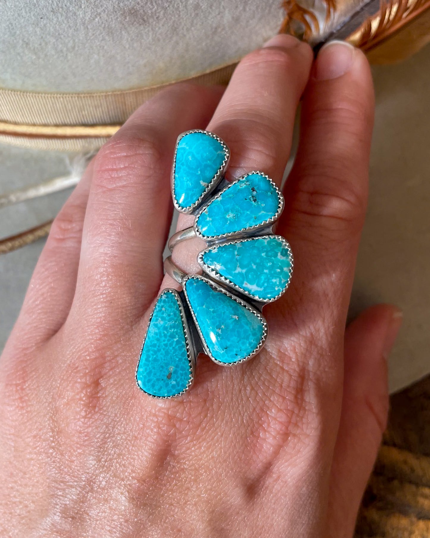 half cluster ring design with small turquoise at the top arcing around to largest turquoise at the bottom modeled on hand