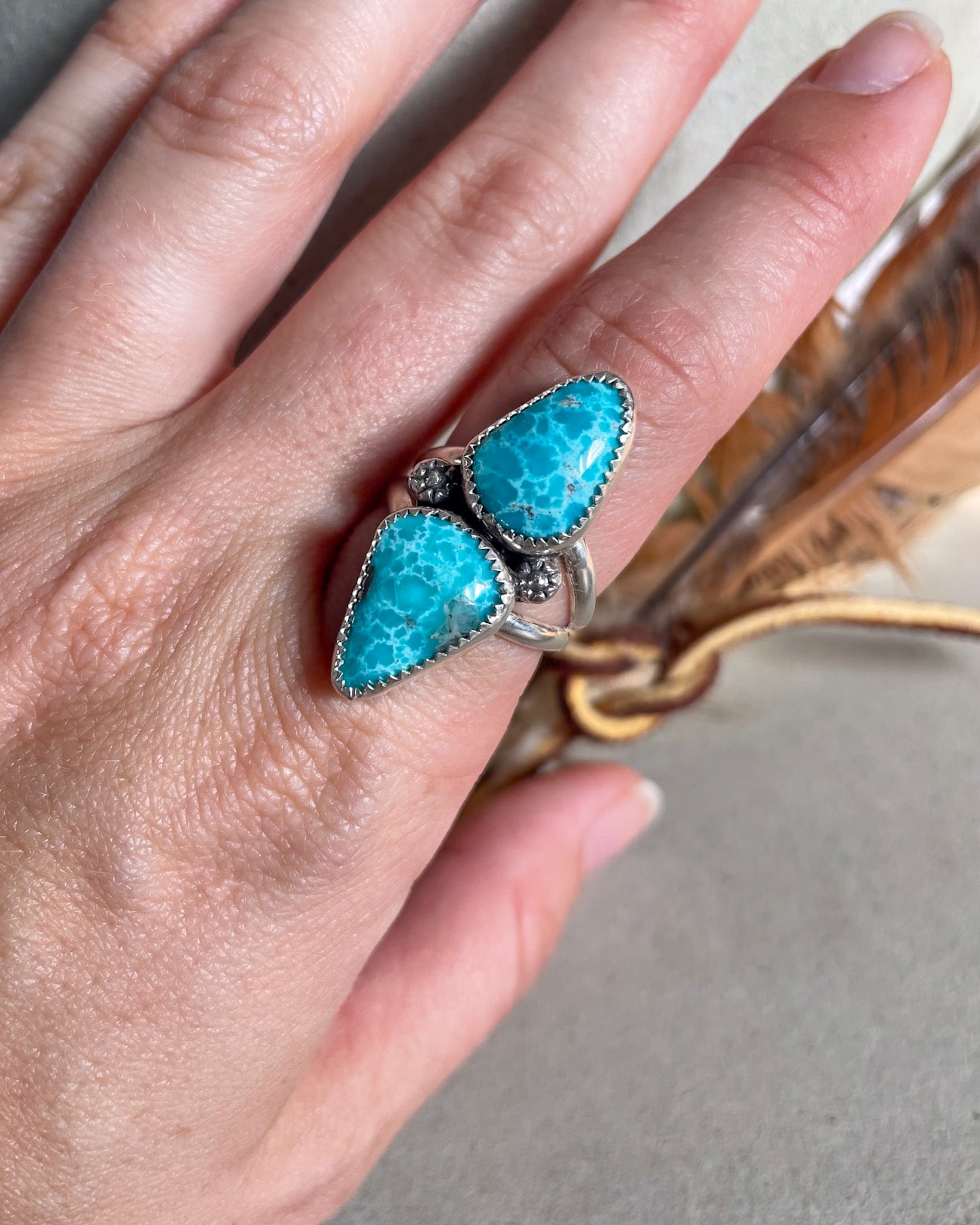 Hand wearing a turquoise ring with silver accents on a neutral background