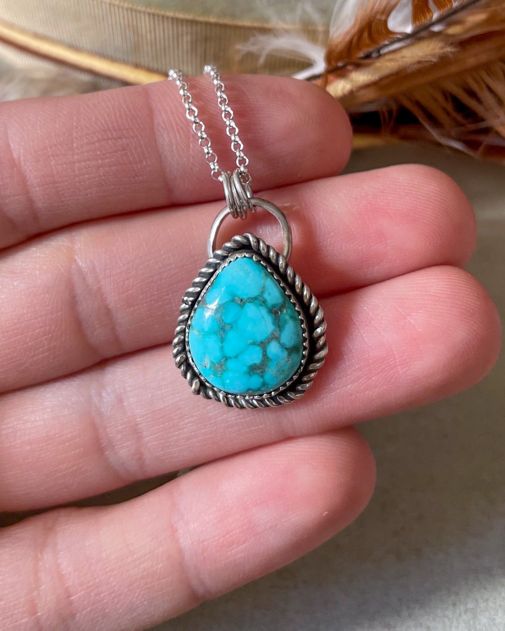 Turquoise pendant necklace held in hand with twisted border